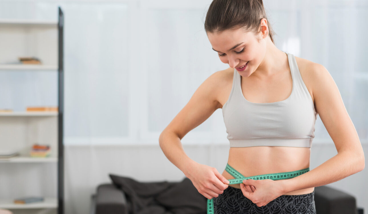 Smiling woman measuring waist after personalized weight loss care in Ellicott MD
