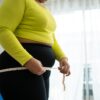 Woman in workout clothes measuring her waist representing the frustration of hitting a weight loss plateau