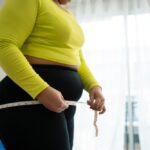 Woman in workout clothes measuring her waist representing the frustration of hitting a weight loss plateau
