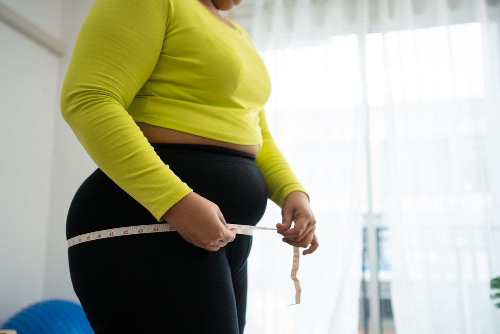 Woman in workout clothes measuring her waist representing the frustration of hitting a weight loss plateau