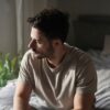 Man sitting on bed looking out window showing signs of testosterone and mental health struggles