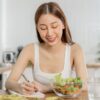 Smiling woman writing notes next to a fresh salad representing mindful eating on GLP-1 medication for better weight loss results