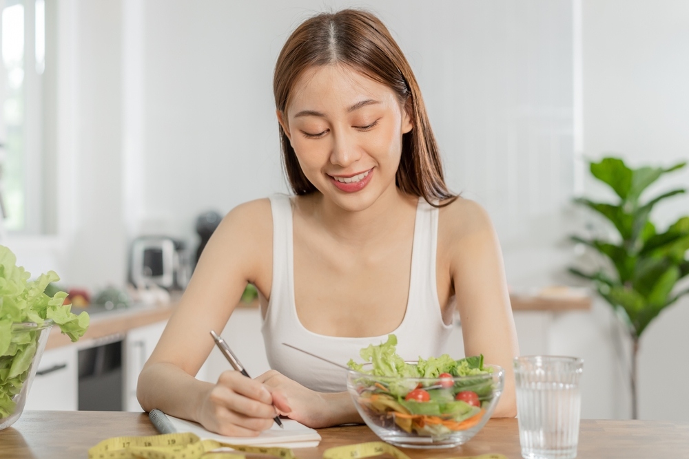 Smiling woman writing notes next to a fresh salad representing mindful eating on GLP-1 medication for better weight loss results