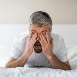 Tired older man sitting on bed covering his face with both hands representing fatigue and mood changes from stopping TRT