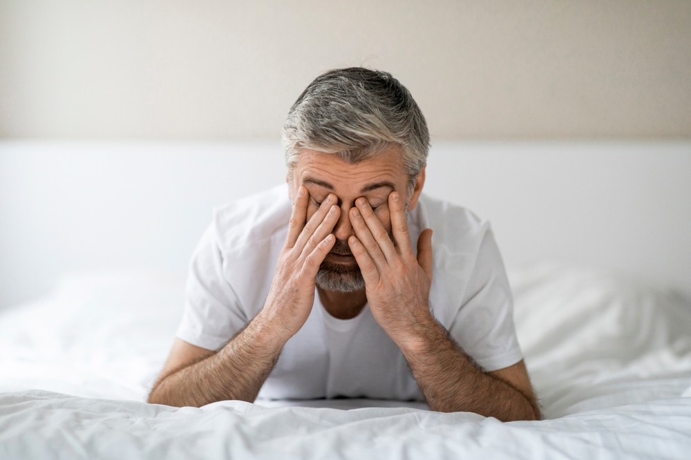 Tired older man sitting on bed covering his face with both hands representing fatigue and mood changes from stopping TRT