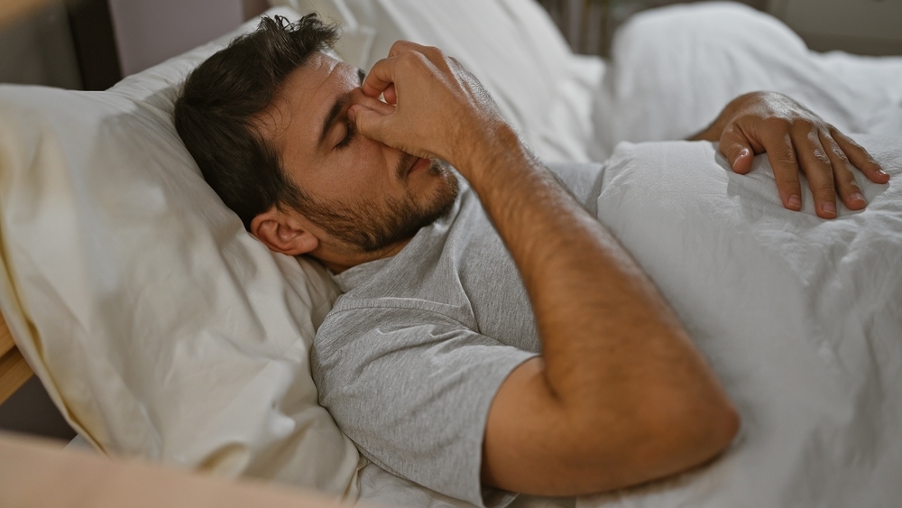Young man lying in bed with restless sleep representing how poor sleep and testosterone quality